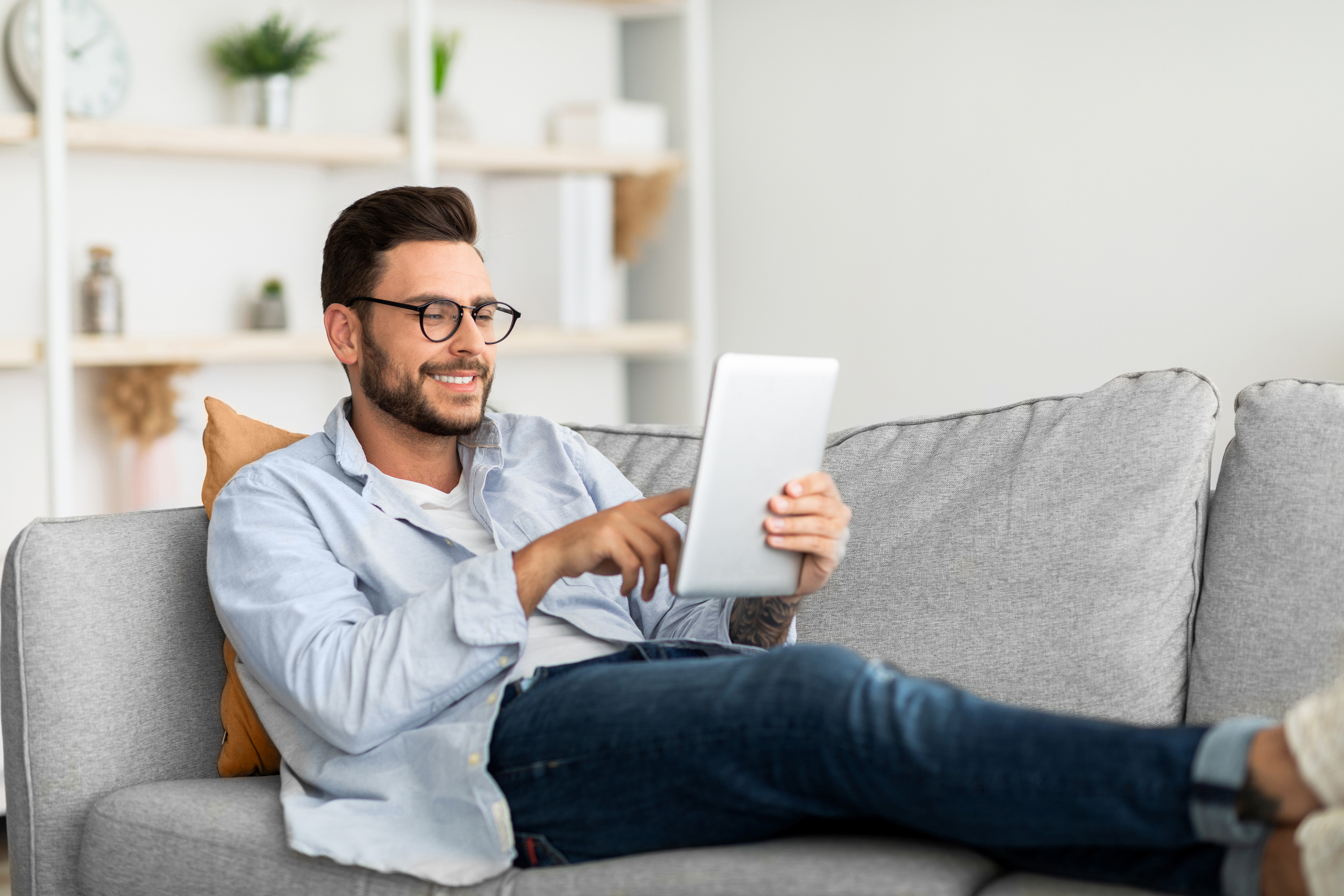 Ein Mann mit einem iPad sitzt auf dem Sofa.